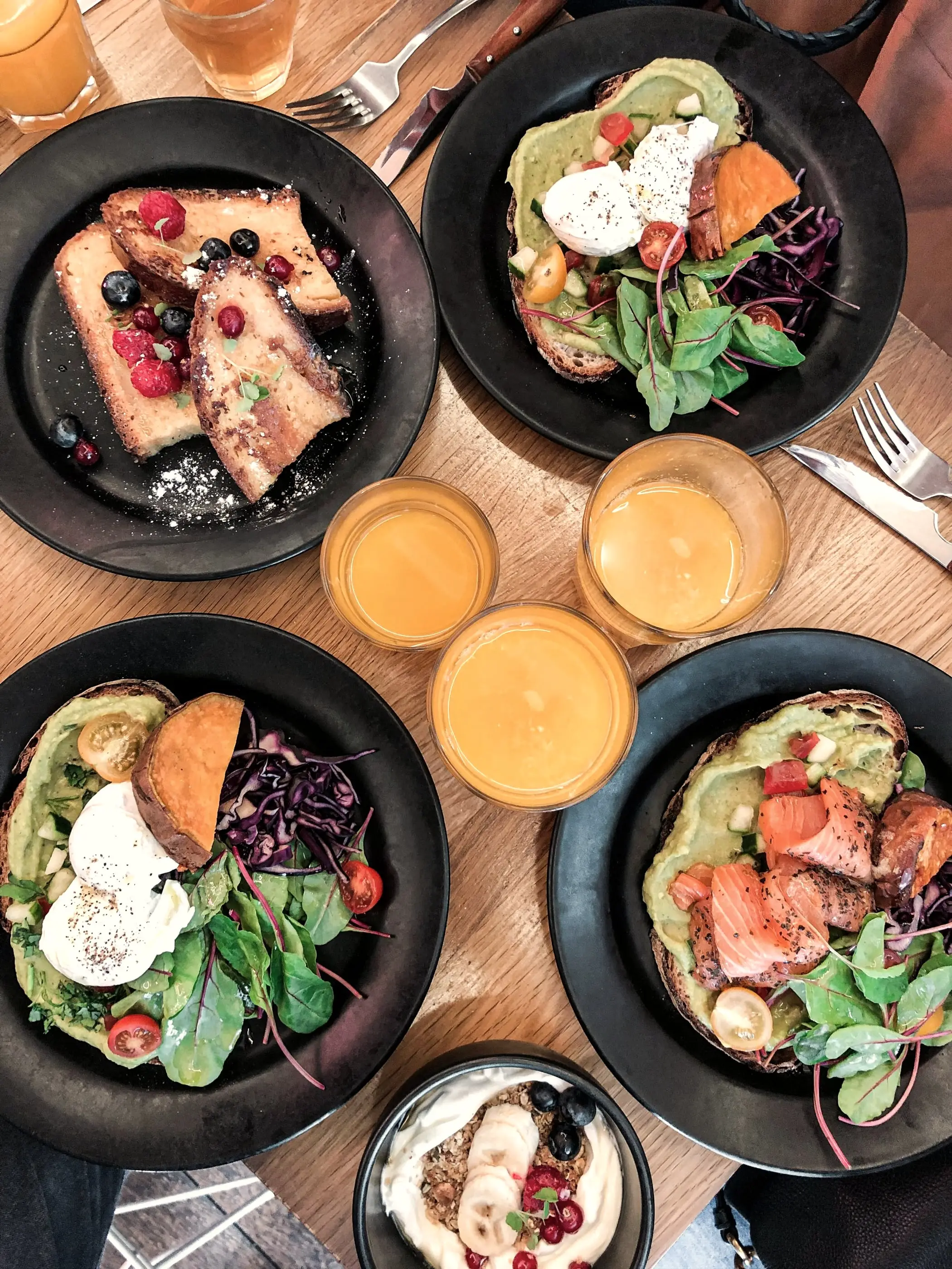 Fyra brunchtallrikar och glas med juice sedda uppifrån.