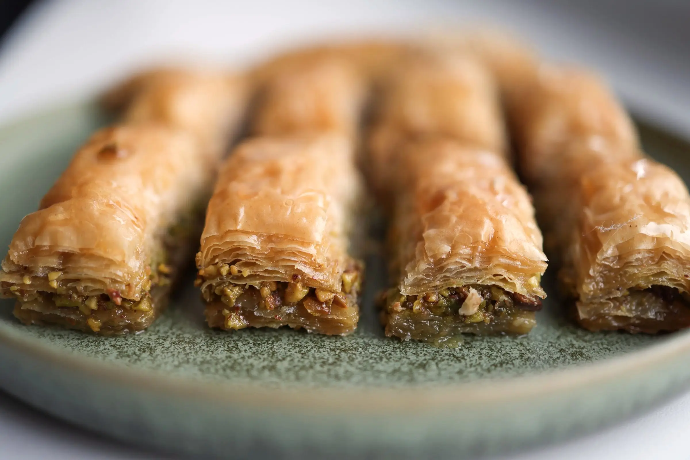 Baklava med pistage på ett grönt fat, i närbild.
