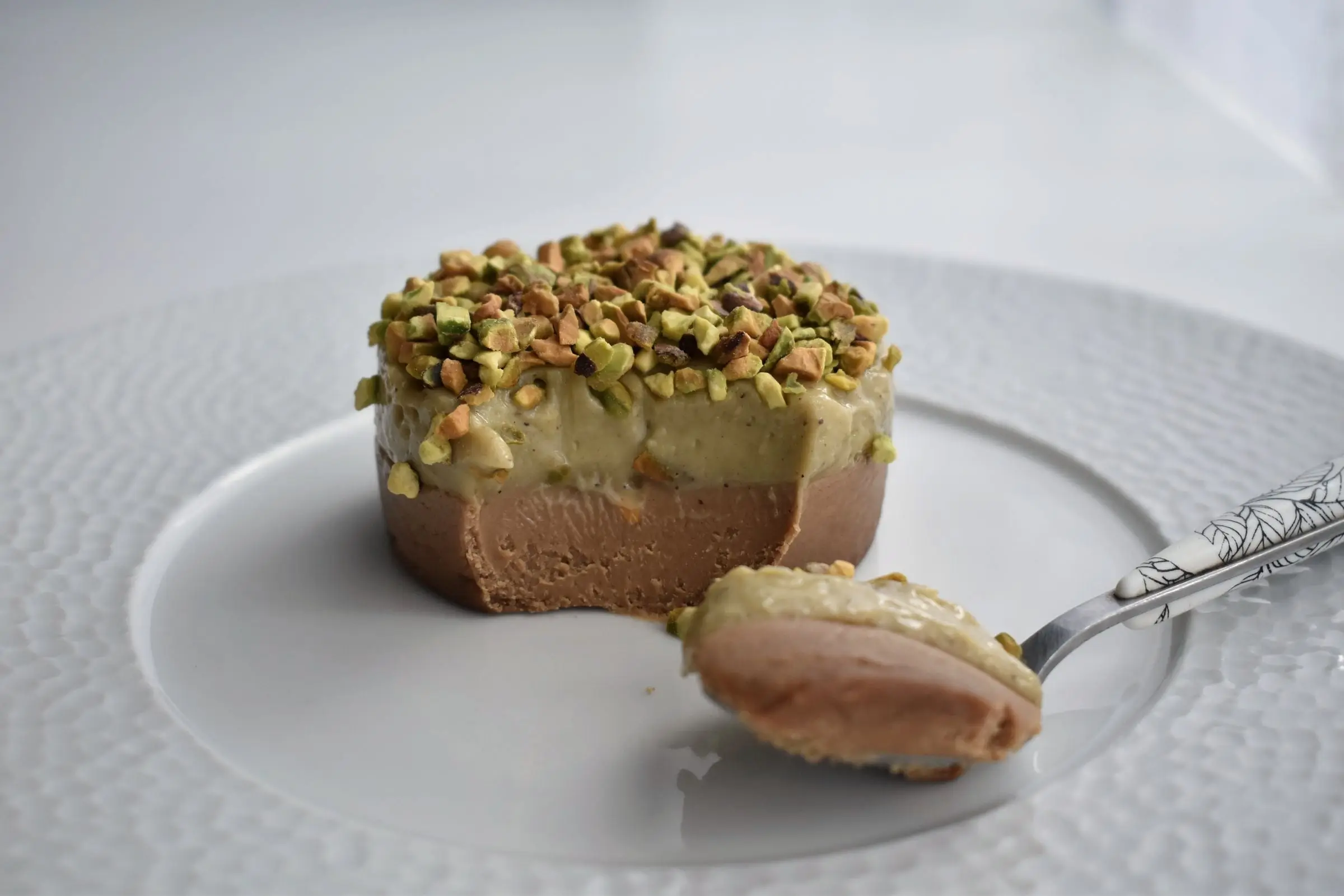 En liten dessert med pistagetäcke på en vit tallrik.