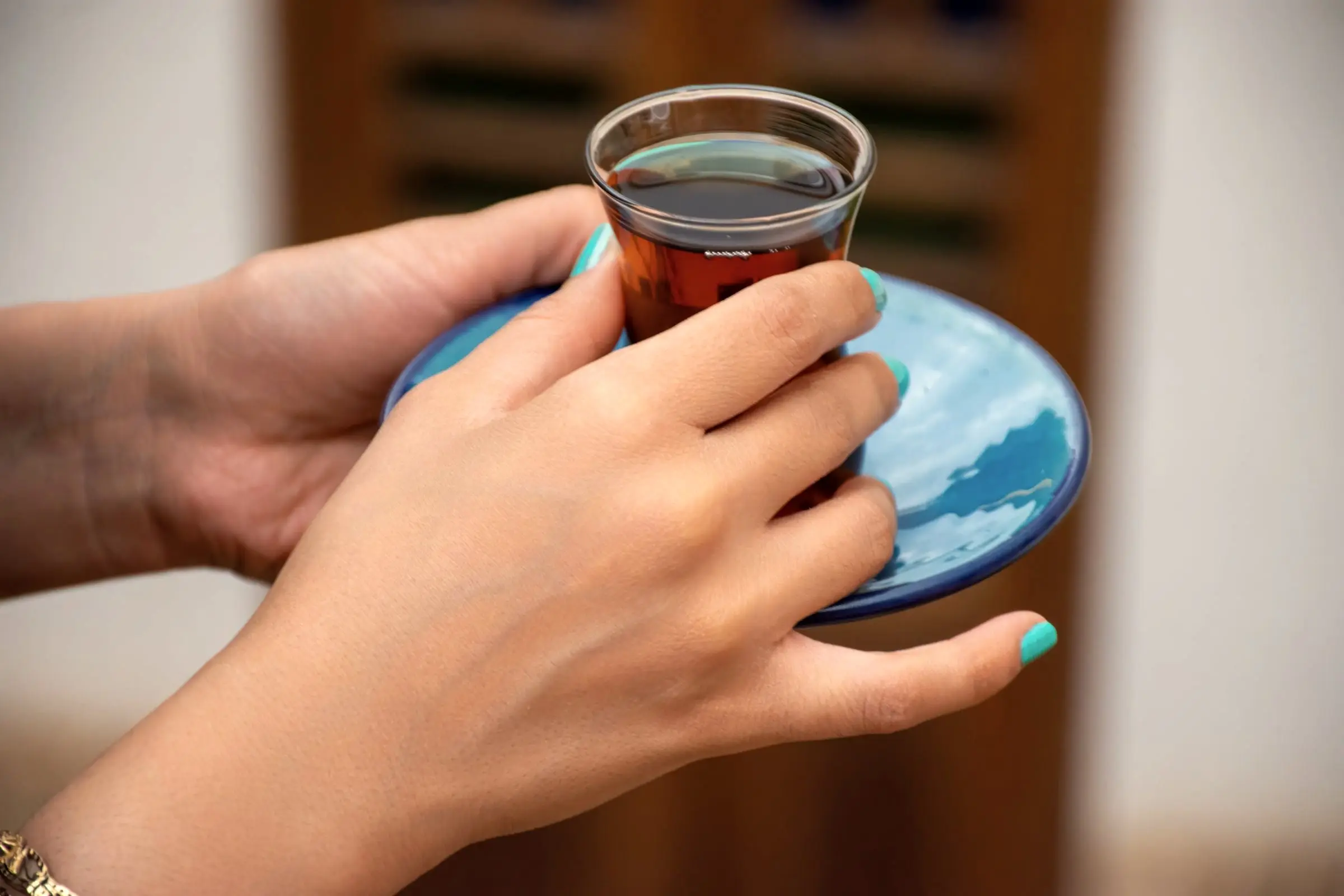 Två händer som håller ett glas te på ett blått fat.